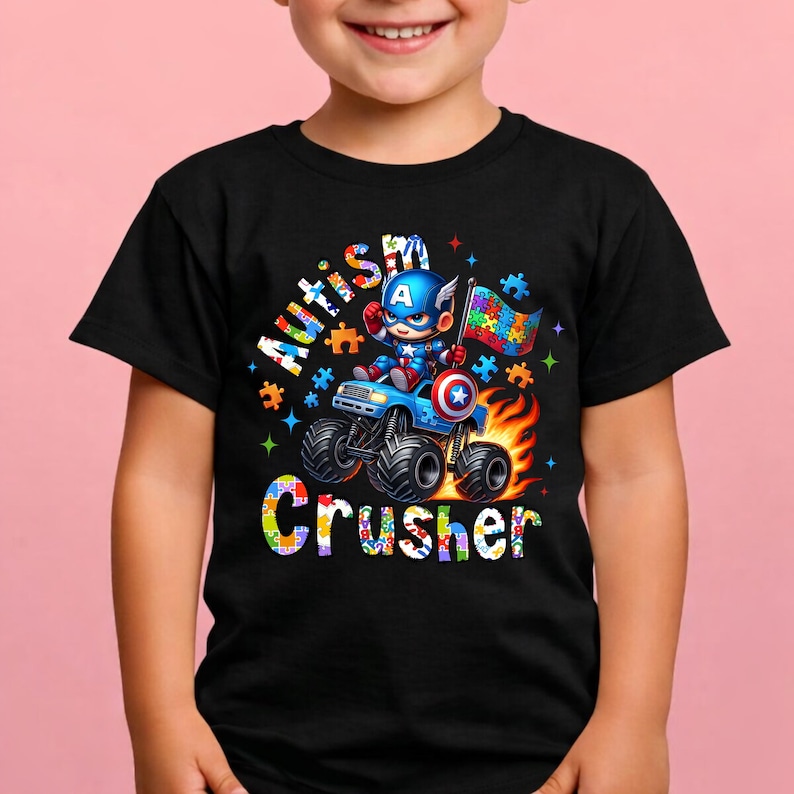 Puede incluir: Camiseta negra con un personaje de dibujos animados del Capit&aacute;n Am&eacute;rica conduciendo un cami&oacute;n monstruo azul. La camiseta tiene las palabras "Autism Crusher" y una bandera de rompecabezas. El dise&ntilde;o incluye llamas y piezas de rompecabezas coloridas.