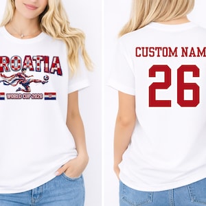 May include: White t-shirt featuring the word "CROATIA" in a red and white checkered design, with a soccer player graphic and the text "WORLD CUP 2026." The back of the shirt displays "CUSTOM NAME" and the number "26" in red.