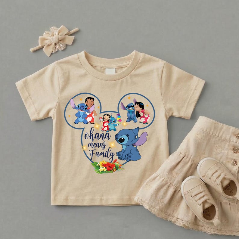 May include: A beige short-sleeved t-shirt featuring a graphic of Stitch and Lilo inside a Mickey Mouse ear outline with the text Ohana means Family, accompanied by a matching beige hair bow and a beige tiered skirt with two beige sneakers.
