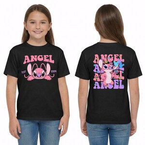 May include: A black t-shirt featuring a pink Angel character graphic. The front displays the text ANGEL EST 2004. The back shows a larger Angel graphic surrounded by repeating text and small colourful flower icons in pink, blue, and yellow hues.