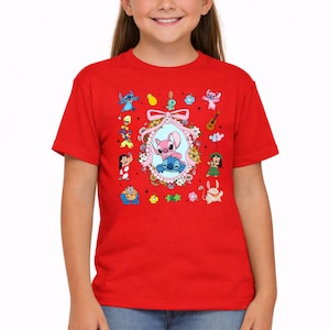 May include: A bright red short-sleeved t-shirt featuring a central oval frame decorated with flowers and a pink bow. Inside the frame are two blue and pink cartoon characters. Surrounding the frame are various small colorful cartoon icons and figures.