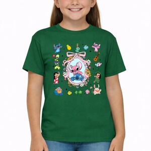 May include: A dark green short-sleeve t-shirt featuring a central oval frame decorated with flowers and a pink bow, containing illustrations of Stitch and Angel. The surrounding area includes various small character icons and tropical motifs.