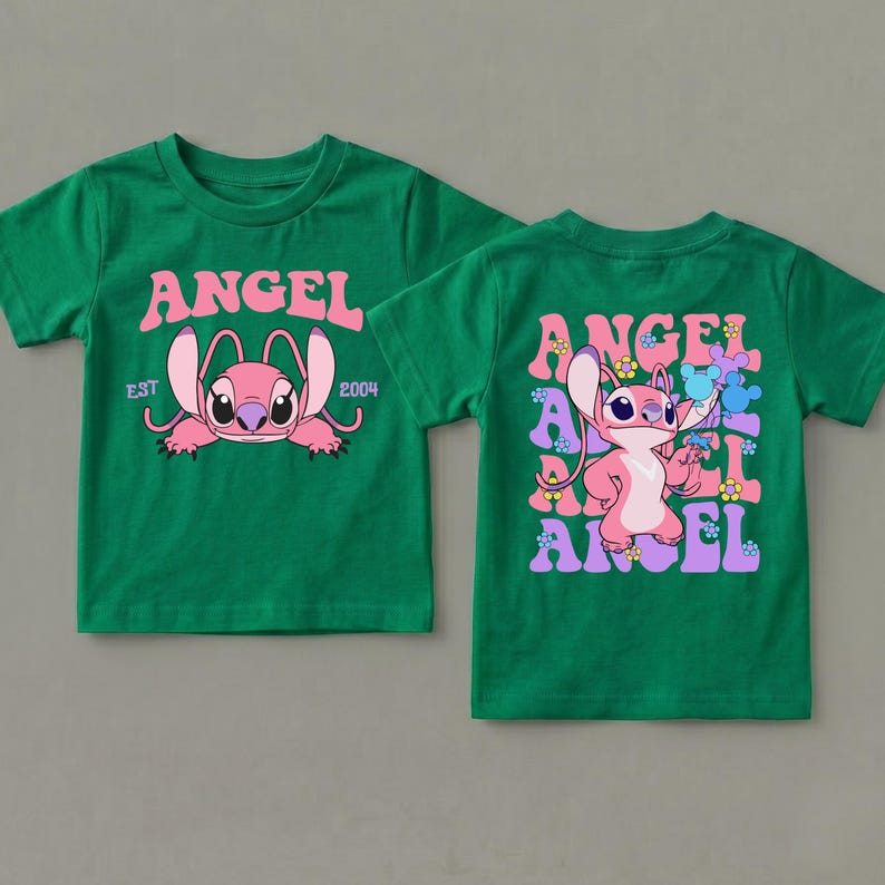 May include: A green short-sleeved t-shirt featuring a pink character graphic. The front displays the text ANGEL EST 2004. The back shows the character Angel surrounded by repeating ANGEL text, small flowers, and blue mouse-ear silhouettes.
