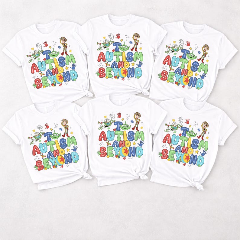 Op de afbeelding: Zes witte t-shirts met een kleurrijk grafisch ontwerp. Het ontwerp bevat de tekst "AUTISM AND BEYOND" in verschillende kleuren, samen met stripfiguren. De shirts zijn korte mouwen en hebben een ronde hals.