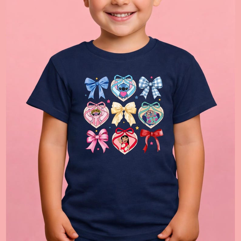 May include: A navy blue short-sleeve t-shirt featuring a central graphic print of various bows and heart-shaped frames. The design includes illustrations of Stitch, Angel, and Lilo from Lilo and Stitch, interspersed with colorful ribbons and small stars.