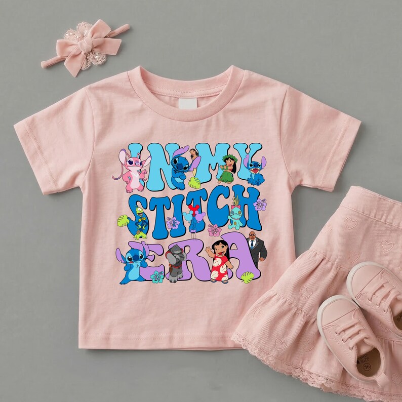 Pode incluir: Uma t-shirt de manga curta rosa claro com uma impress&atilde;o gr&aacute;fica com o texto IN MY STITCH ERA, rodeada por v&aacute;rias personagens de desenhos animados, incluindo Stitch, Angel e Lilo, acompanhada por uma fita para o cabelo e saia rosa.