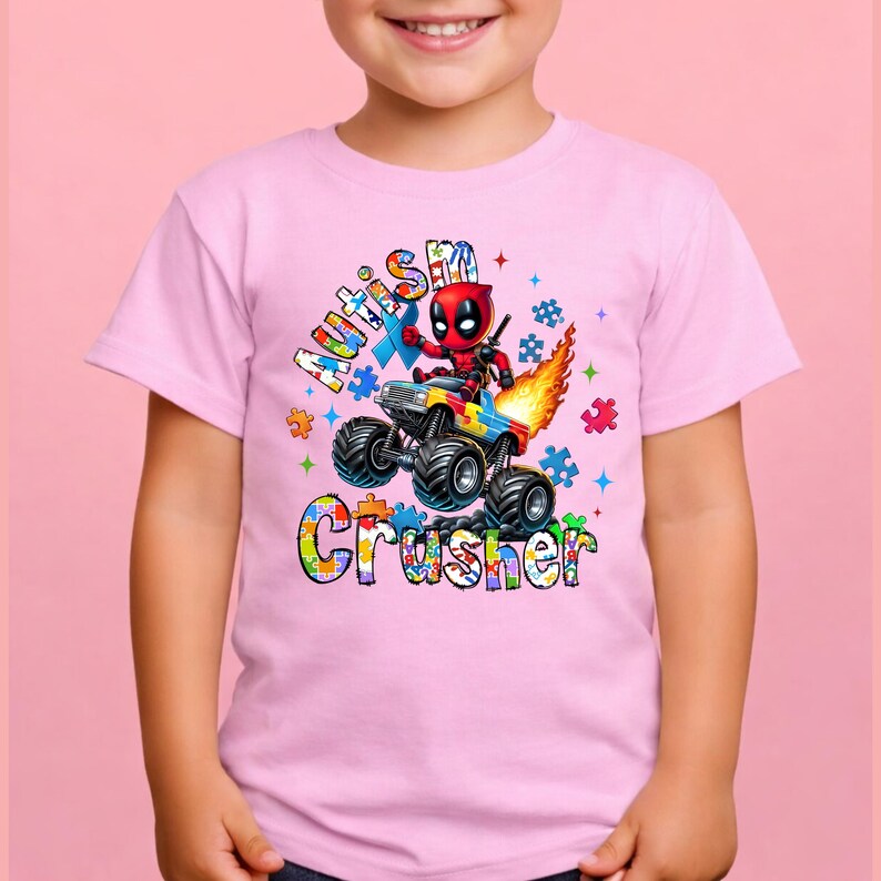 Puede incluir: Camiseta rosa con un gr&aacute;fico colorido de un monster truck y un personaje similar a Deadpool. El texto en la camiseta dice "Autism Crusher" en un dise&ntilde;o vibrante y multicolor, con piezas de rompecabezas y estrellas.