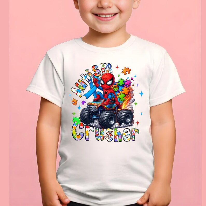 Puede incluir: Camiseta blanca con un gr&aacute;fico colorido de Spider-Man en un cami&oacute;n monstruo. El dise&ntilde;o incluye las palabras "Autism Crusher" y piezas de rompecabezas. La camiseta es de manga corta.