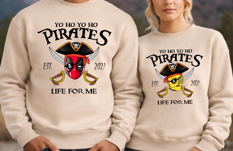 K&ouml;nnte beinhalten: Beige Sweatshirts mit Piratenmotiv. Das Design zeigt einen Piratenhut, gekreuzte Schwerter und den Text "YO HO YO HO PIRATES EST. 2022 LIFE FOR ME." Ein Sweatshirt hat einen von Deadpool inspirierten Piraten, das andere einen gelben Piraten.