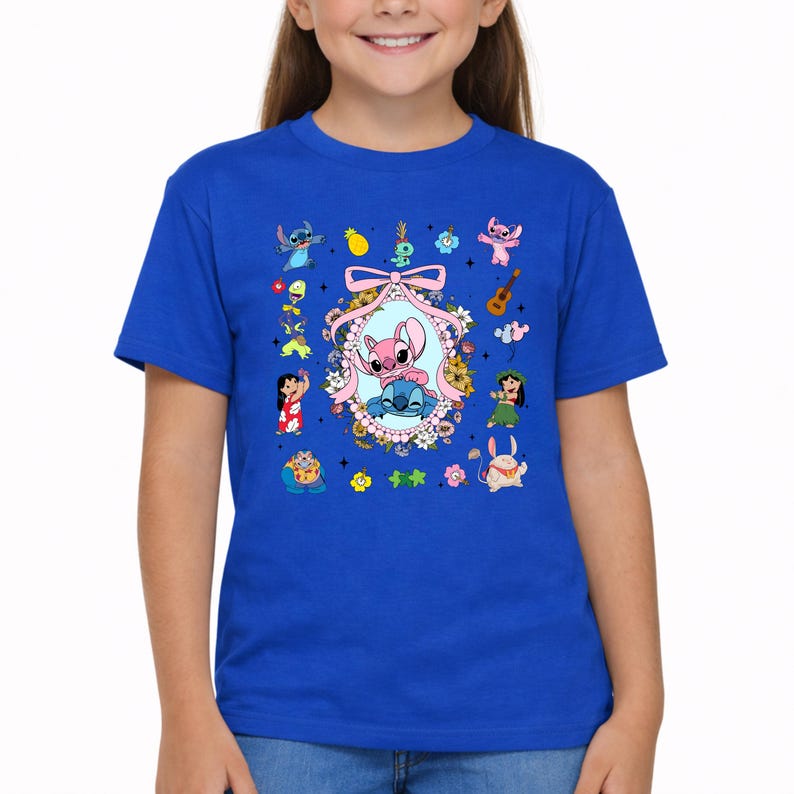 May include: A royal blue short-sleeved t-shirt featuring a central oval frame decorated with flowers and a pink ribbon. Inside the frame are the characters Stitch and Angel. Surrounding the frame are various small illustrations of characters, a pineapple, a guitar, and flowers.