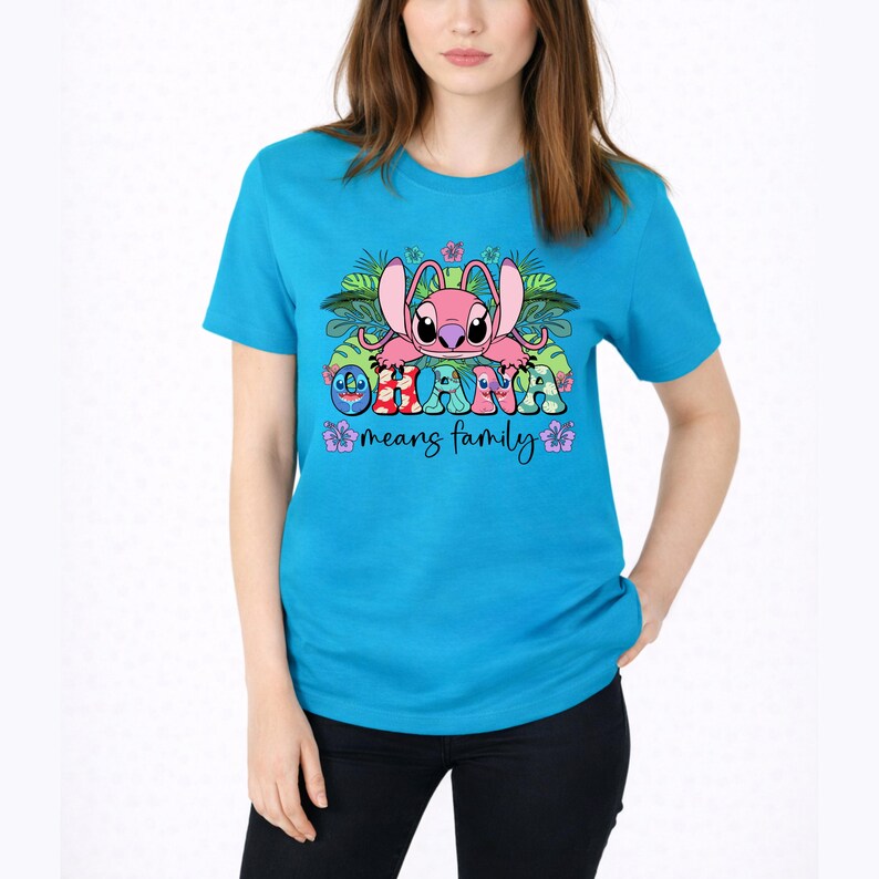 May include: A bright turquoise short-sleeve t-shirt featuring a graphic of a pink alien character surrounded by tropical leaves and flowers. The text "OHANA" is printed in colorful patterned letters above the script text "means family".