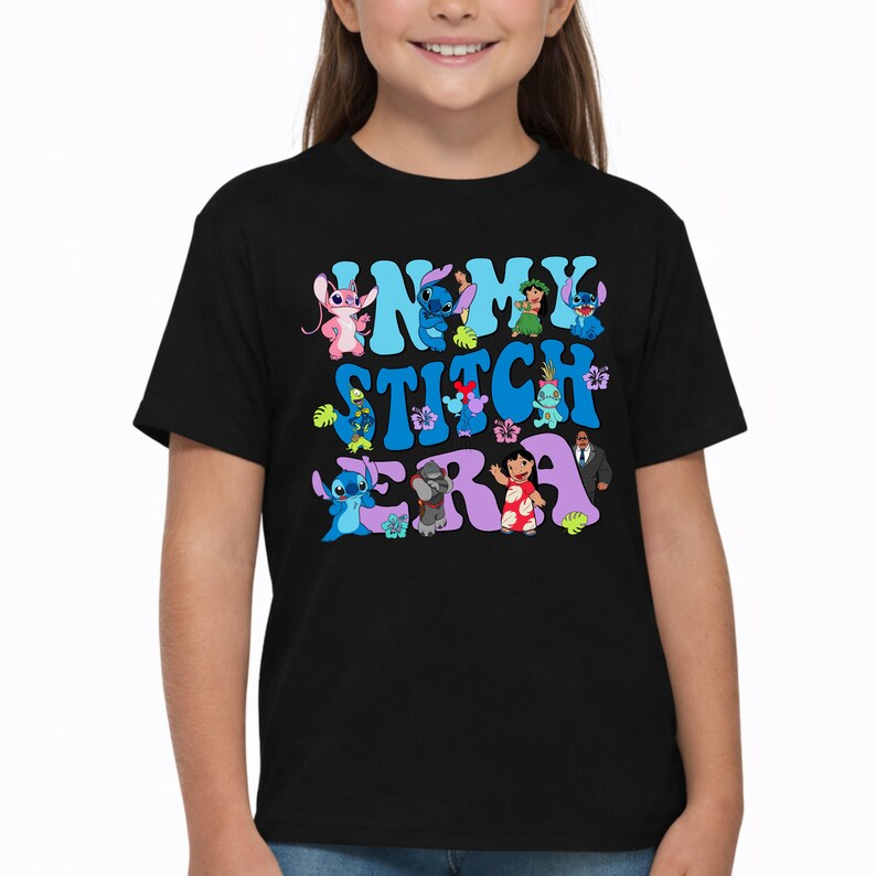 Pode incluir: Uma t-shirt preta de manga curta com uma impress&atilde;o gr&aacute;fica colorida com o texto IN MY STITCH ERA. O design inclui v&aacute;rias personagens animadas da franquia Lilo e Stitch, intercaladas com flores e folhas tropicais.