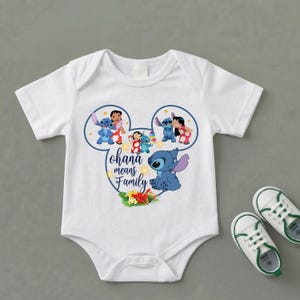 May include: A white short-sleeve baby bodysuit featuring a graphic of Stitch and Lilo inside a Mickey Mouse ear outline. The text reads Ohana means Family, accompanied by colorful tropical flowers and small yellow stars on the front center.