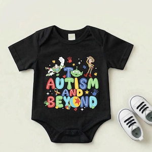 Op de afbeelding: Zwarte babybody met de tekst "Autism and Beyond" in kleurrijke letters, met stripfiguren en handafdrukken. Witte babyschoenen met zwarte veters.