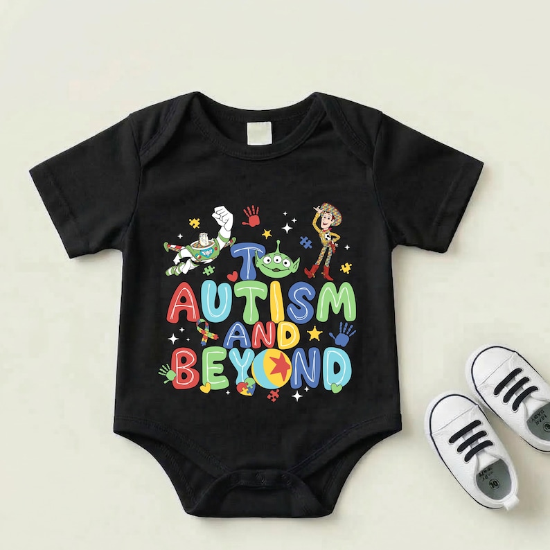 Op de afbeelding: Zwarte babybody met de tekst "Autism and Beyond" in kleurrijke letters, met stripfiguren en handafdrukken. Witte babyschoenen met zwarte veters.