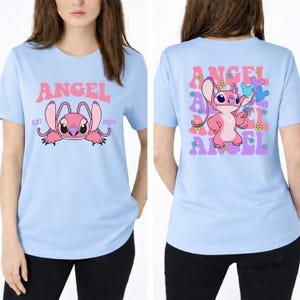 May include: A light blue t-shirt featuring a graphic of the pink character Angel on the front with the text ANGEL EST 2004. The back displays a larger graphic of Angel holding balloons surrounded by repeating text and small colourful flower icons.