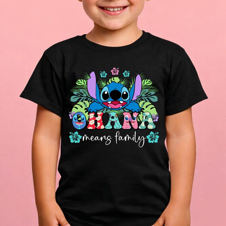 May include: A black t-shirt featuring a graphic of the blue character Stitch surrounded by green tropical leaves and colorful hibiscus flowers. The text OHANA is printed in patterned letters, with the phrase means family written below in white.