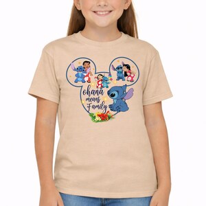 May include: A light tan short-sleeve t-shirt featuring a dark blue Mickey Mouse ear outline graphic. Inside the outline are illustrations of Lilo and Stitch, with the text "ohana means Family" in a cursive font and a cluster of tropical flowers.