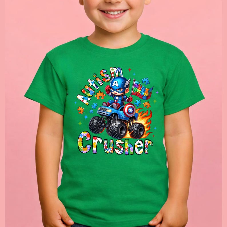 Puede incluir: Camiseta verde con un gr&aacute;fico de un superh&eacute;roe conduciendo un monster truck. El dise&ntilde;o incluye las palabras "Autism Crusher" y una bandera con patrones de piezas de rompecabezas. El superh&eacute;roe lleva un traje azul y rojo.