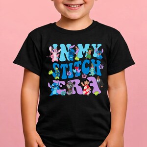 Pode incluir: Uma t-shirt preta de manga curta com uma impress&atilde;o gr&aacute;fica com o texto IN MY STITCH ERA. O design inclui v&aacute;rias personagens coloridas de desenhos animados da franquia Lilo e Stitch, incluindo Stitch, Angel, Lilo e outros, intercalados com flores e folhas tropicais.