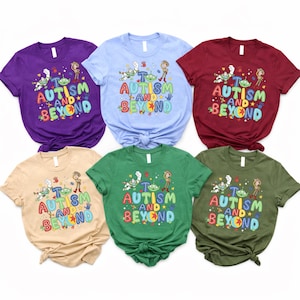 Op de afbeelding: Zes T-shirts met korte mouwen in verschillende kleuren, waaronder paars, blauw, bordeauxrood, beige, groen en olijfgroen. Elk shirt heeft de tekst "To Autism and Beyond" met cartoonkarakterafbeeldingen.