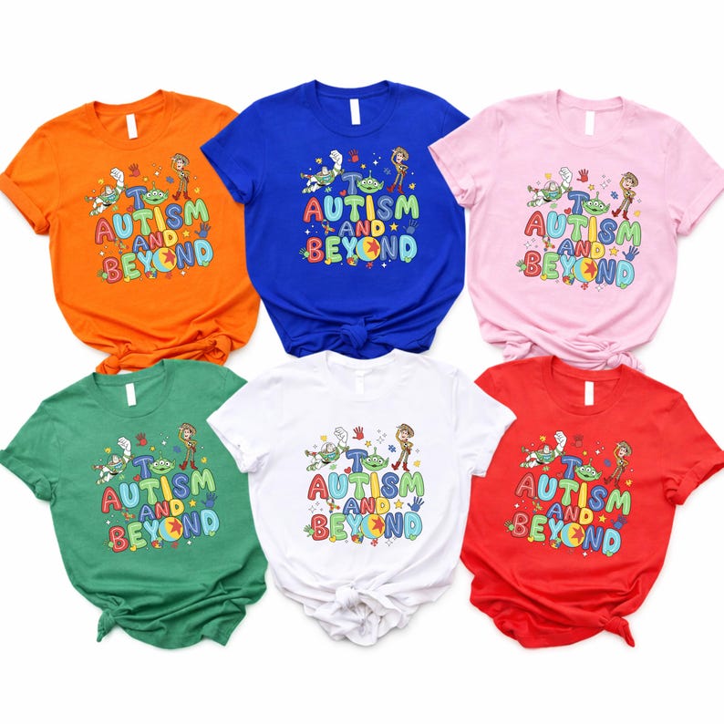 Op de afbeelding: Zes shirts met korte mouwen in oranje, blauw, roze, groen, wit en rood. Elk shirt toont de tekst "AUTISM AND BEYOND" met stripfiguren. De shirts zijn gemaakt van een zacht materiaal.