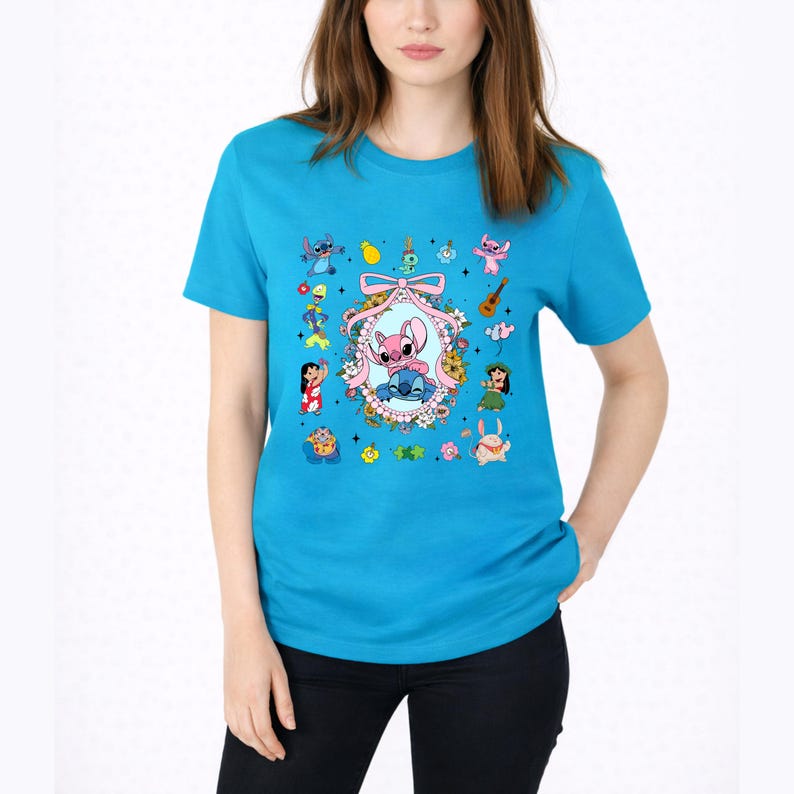 May include: A bright turquoise short-sleeve t-shirt featuring a central graphic of a pink and blue alien character inside a floral oval frame with a pink bow. Surrounding the frame are various small cartoon characters, flowers, and icons.