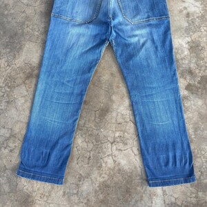 May include: Faded blue denim jeans with a classic five-pocket design. The jeans have a straight leg cut and show signs of wear, with subtle fading and creases. The back pockets are visible, and the jeans are laid flat.