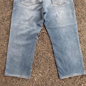 May include: Light blue denim jeans with a classic five-pocket design. The jeans have a straight leg cut and show signs of wear. The back pockets are visible, and the fabric has a faded appearance.