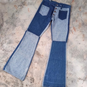 May include: Two-tone denim jeans with a button fly and two front pockets. The jeans feature a patchwork design with light and dark blue denim panels. The legs flare out from the knee, creating a bell-bottom style.
