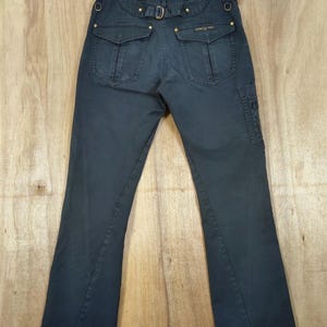 Pu&ograve; includere: Pantaloni blu navy scuro con tasche multiple e cintura. I pantaloni hanno un design a gamba svasata e dettagli dorati. Il retro presenta due tasche con patta e una cintura con fibbia. I pantaloni sono appesi a una gruccia di legno.