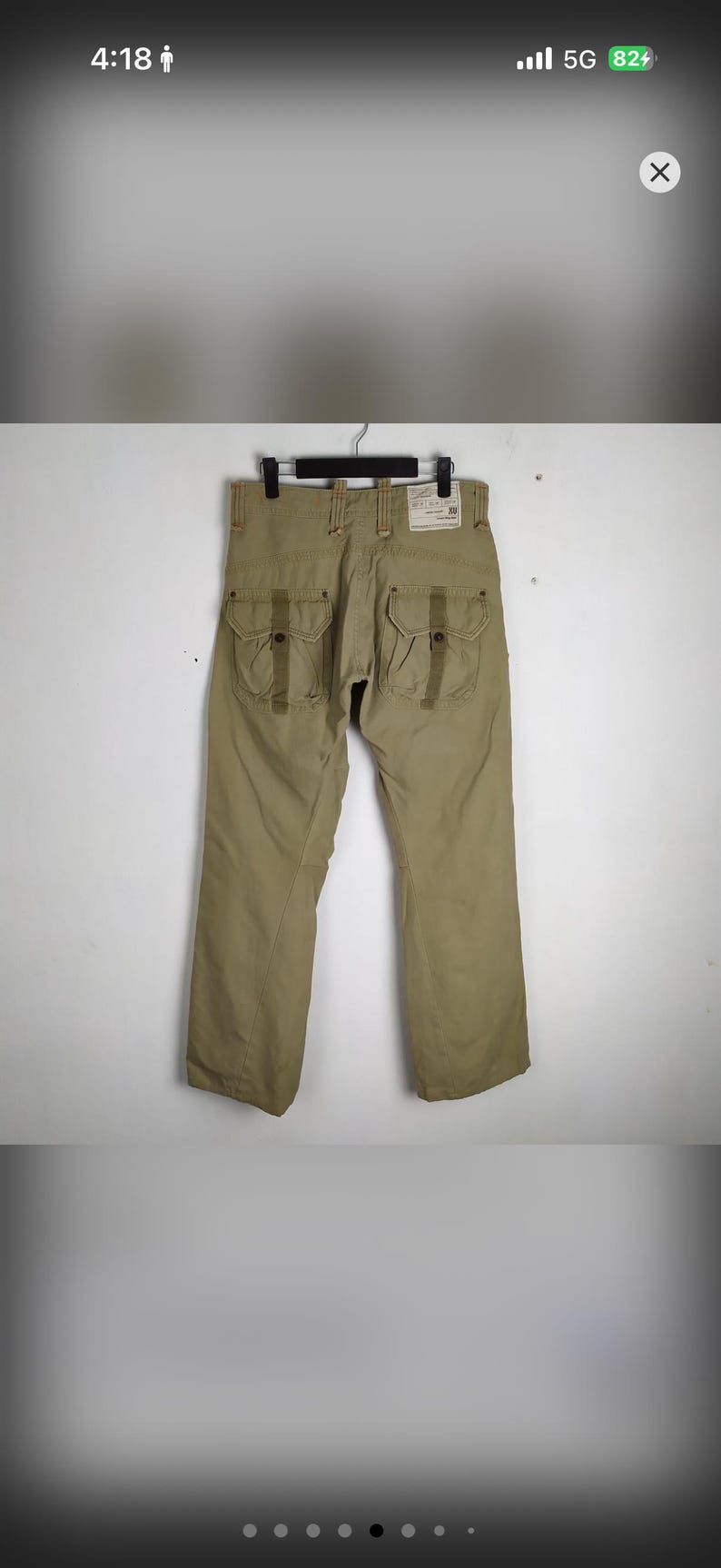 May include: Khaki-colored cargo pants with multiple pockets and a straight leg design. The pants are hanging on a black hanger against a neutral background. The back of the pants is visible, showcasing the pocket details.