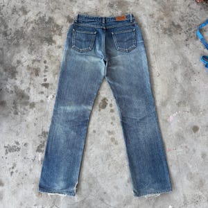 May include: Faded blue denim jeans with a classic five-pocket design. The jeans have a straight leg cut and a worn appearance, with visible fading and distressing. A brown leather patch is visible on the back waistband.