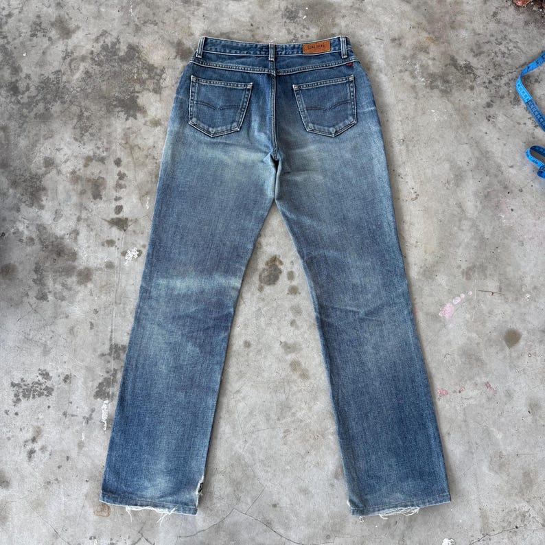 May include: Faded blue denim jeans with a classic five-pocket design. The jeans have a straight leg cut and a worn appearance, with visible fading and distressing. A brown leather patch is visible on the back waistband.