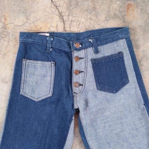 May include: Two-tone denim jeans with a button-up fly and two front pockets. The jeans feature a contrasting design, with one side in a darker blue and the other in a lighter blue wash.