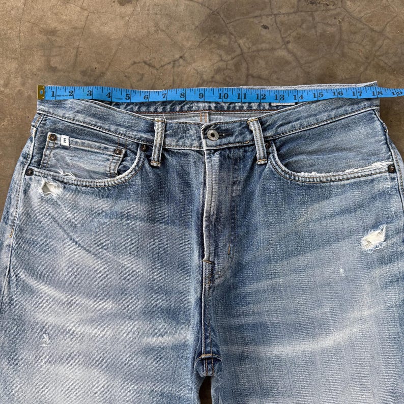 Pu&ograve; includere: Jeans in denim blu chiaro con chiusura a bottone e dettagli strappati. La vita misura circa 43 cm di larghezza. Presenta un classico stile a cinque tasche e un lavaggio sbiadito.