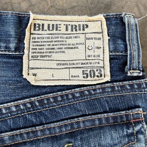May include: Close-up of blue denim jeans with a visible label. The label reads "BLUE TRIP" and includes text about the brand and product details. The jeans have visible stitching and a "503" label.