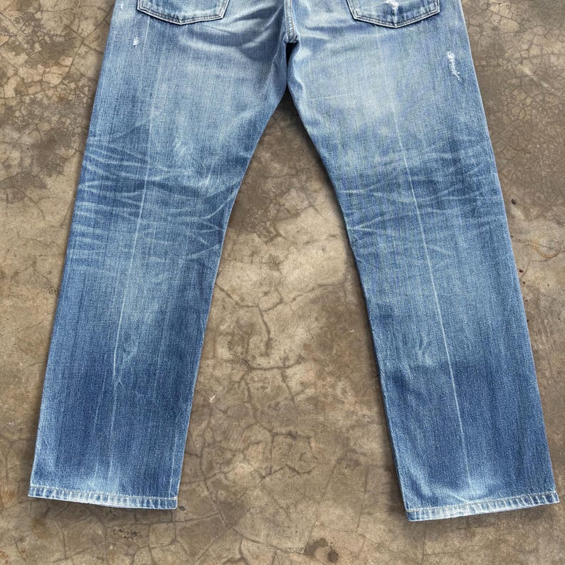 Pu&ograve; includere: Jeans in denim blu chiaro con lavaggio sbiadito e dettagli usurati. I jeans hanno un classico design a cinque tasche e una vestibilit&agrave; dritta. Il denim mostra segni di usura, aggiungendo all'estetica vintage.