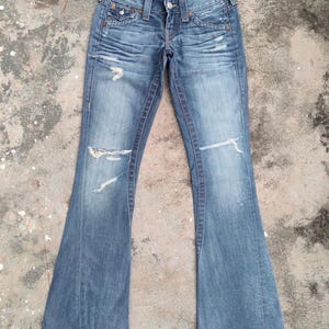 May include: Faded blue denim jeans with a flared leg design. The jeans feature distressed details, including rips on the knees and fading throughout. Classic five-pocket styling with a button and zip closure.