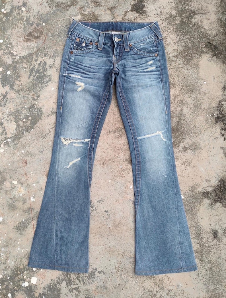 May include: Faded blue denim jeans with a flared leg design. The jeans feature distressed details, including rips on the knees and fading throughout. Classic five-pocket styling with a button and zip closure.