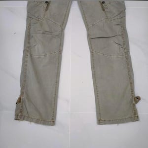 May include: A pair of olive green cargo pants with multiple pockets and reinforced knee panels. The pants have a relaxed fit and feature adjustable straps at the ankles. The fabric appears to be a durable cotton blend.