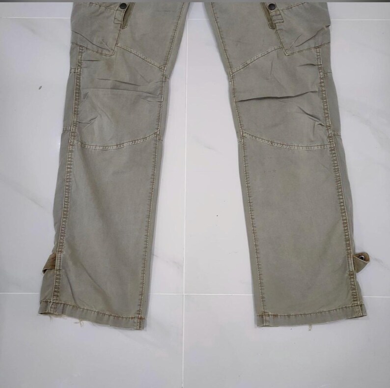 May include: A pair of olive green cargo pants with multiple pockets and reinforced knee panels. The pants have a relaxed fit and feature adjustable straps at the ankles. The fabric appears to be a durable cotton blend.