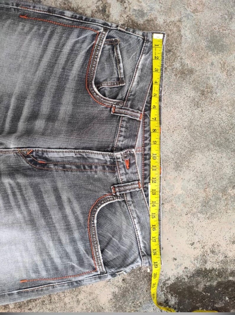 K&ouml;nnte beinhalten: Graue Jeans mit orangefarbenen N&auml;hten. Die Jeans haben ein klassisches F&uuml;nf-Taschen-Design und einen geraden Beinverlauf. Ein gelbes Ma&szlig;band zeigt die L&auml;nge der Jeans, ca. 51 cm.