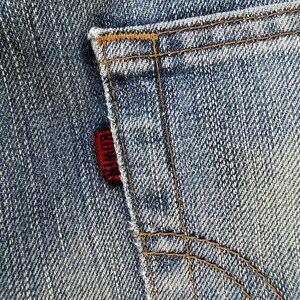 May include: Close-up of a denim jeans pocket with brown stitching. A red tag with the brand name "EDWIN" is visible on the pocket's edge. The jeans have a classic blue wash.