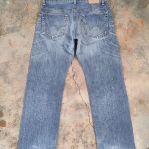 May include: Light blue denim jeans with a faded wash. The jeans feature classic five-pocket styling, belt loops, and a leather patch on the back waistband. The back pockets have a distinctive curved design. The jeans are laid flat.
