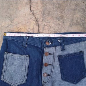 May include: Two-tone denim jeans with a button fly and front pockets. The jeans feature a light blue and dark blue color scheme. A measuring tape shows the waist is approximately 15 inches wide.