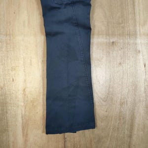 Pu&ograve; includere: Pantaloni blu navy scuro con design a gamba dritta. I pantaloni sono realizzati in un tessuto resistente e presentano uno stile classico e casual. I pantaloni sono mostrati su una superficie di legno marrone chiaro.