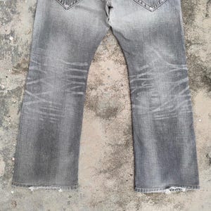 K&ouml;nnte beinhalten: Verblasste graue Jeans mit ausgestelltem Bein. Die Jeans weisen Abnutzungserscheinungen mit abgenutzten Bereichen und Ausbleichen auf. Die unteren S&auml;ume sind ausgefranst.