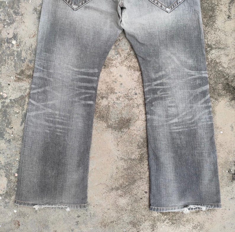 K&ouml;nnte beinhalten: Verblasste graue Jeans mit ausgestelltem Bein. Die Jeans weisen Abnutzungserscheinungen mit abgenutzten Bereichen und Ausbleichen auf. Die unteren S&auml;ume sind ausgefranst.