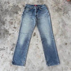 May include: Faded blue denim jeans with a distressed look. The jeans have a classic five-pocket design, a button and zipper closure, and a small rip on the left knee. The jeans are slightly flared at the bottom.